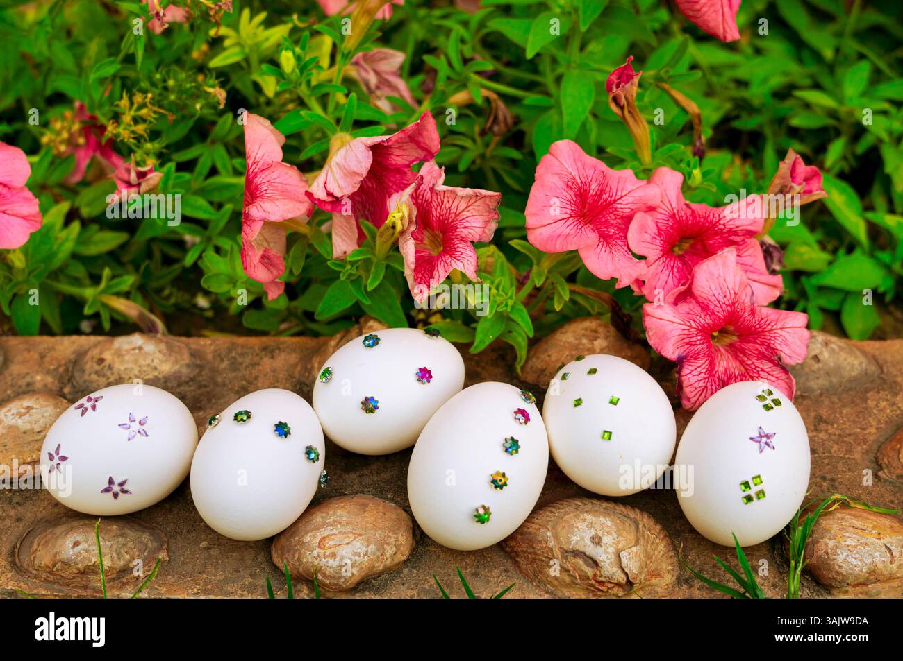 Un affascinante allestimento pasquale con uova bianche decorate immerse nell'erba verde, circondate da elementi floreali, perfetto per biglietti d'auguri, striscioni e holi Foto Stock