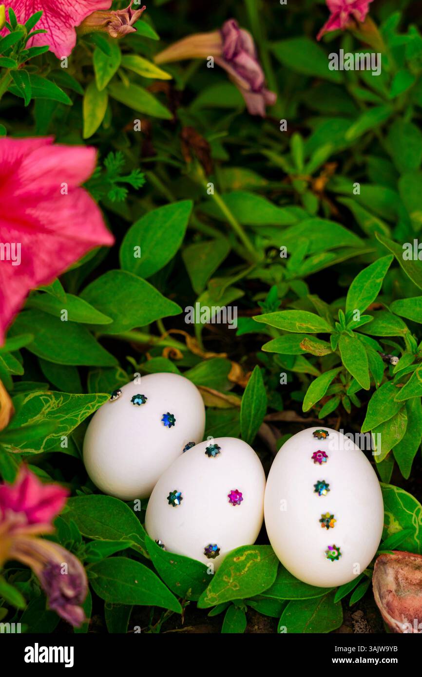 Un affascinante allestimento pasquale con uova bianche decorate immerse nell'erba verde, circondate da elementi floreali, perfetto per biglietti d'auguri, striscioni e holi Foto Stock