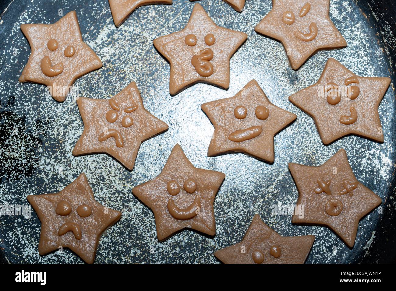 Un vassoio pieno di biscotti appena fatti a forma di stella, ciascuno decorato con espressioni facciali uniche e giocose. I biscotti sono marrone chiaro e vetrina Foto Stock