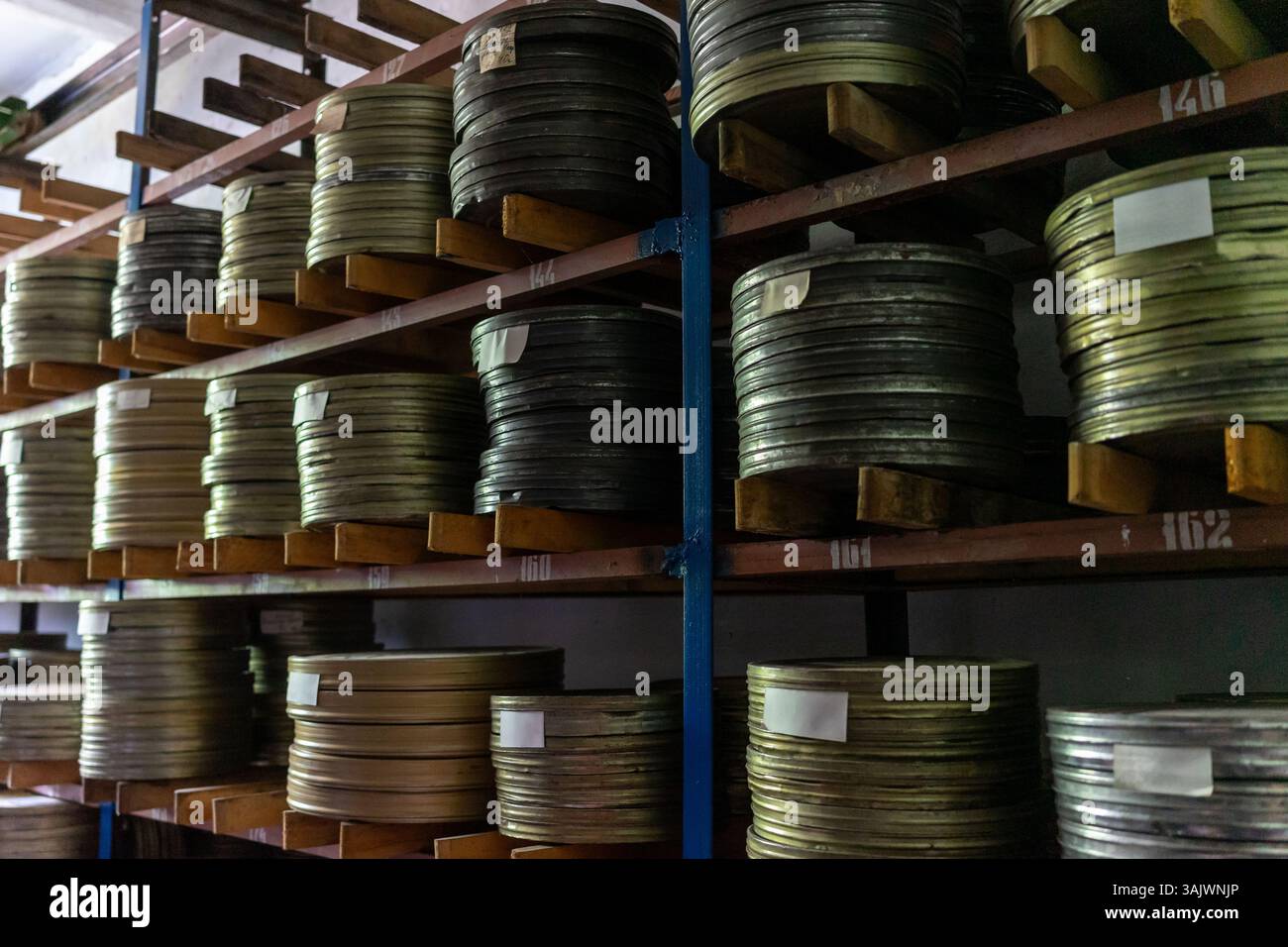 Una grande collezione di bobine di pellicola ordinatamente organizzate su scaffali in legno all'interno di una struttura di archiviazione. La camera è poco illuminata, sottolineando la lucentezza metallica Foto Stock