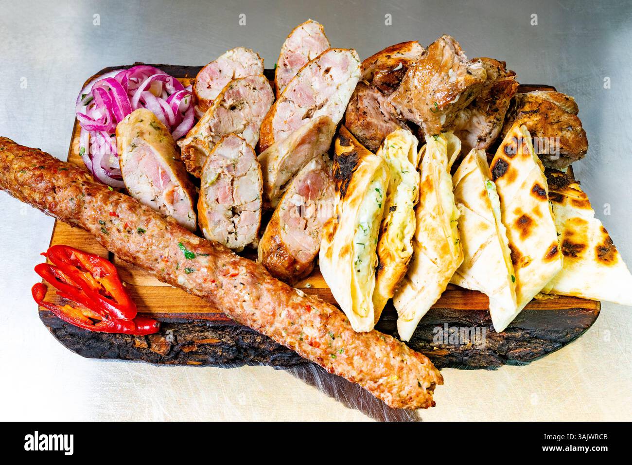 Una vivace mostra di varie carni alla griglia, tra cui spiedini, salsicce e pane servito insieme a cipolle fresche e peperoni, che mostrano un ricco culinario Foto Stock
