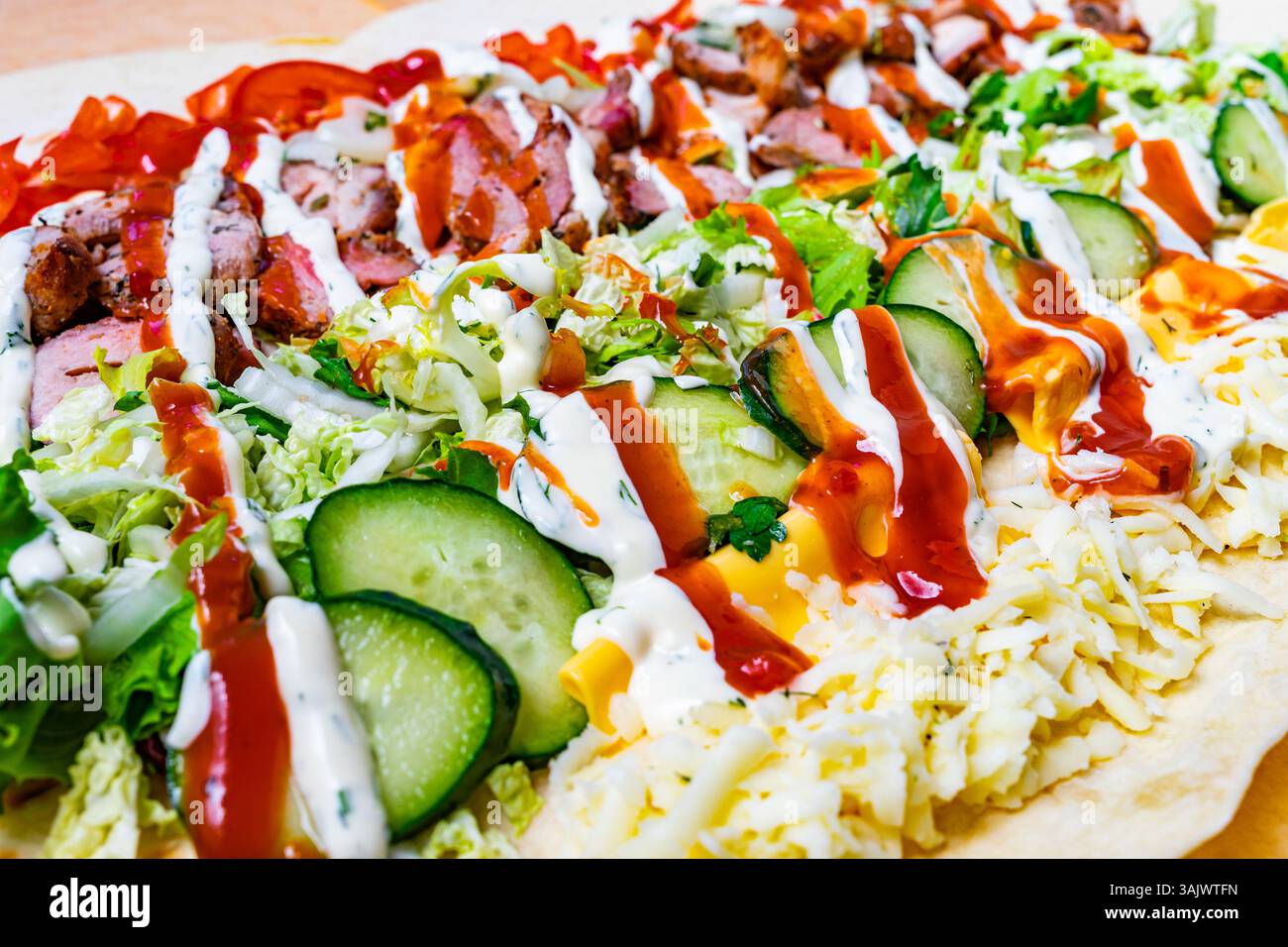 Un avvolgimento vivace presenta strati di carne alla griglia, verdure fresche e salse colorate. Questo piatto appetitoso è perfetto per un pasto veloce o un gustoso sn Foto Stock