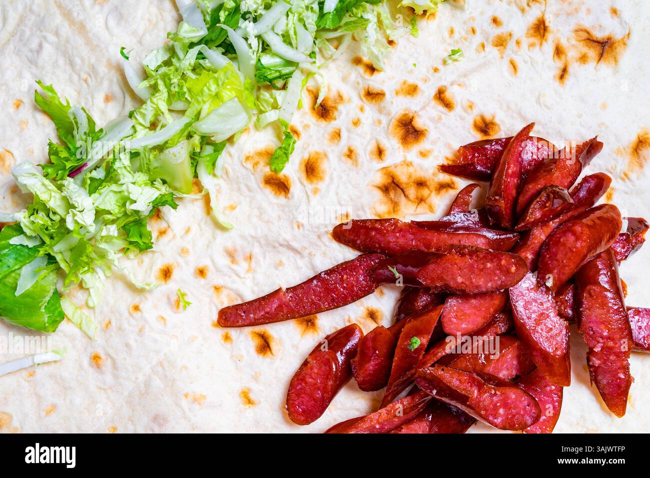La salsiccia a fette è ordinata accanto alla lattuga fresca su una focaccia. I colori vivaci e le texture creano un layout accattivante, perfetto per un gustoso Foto Stock