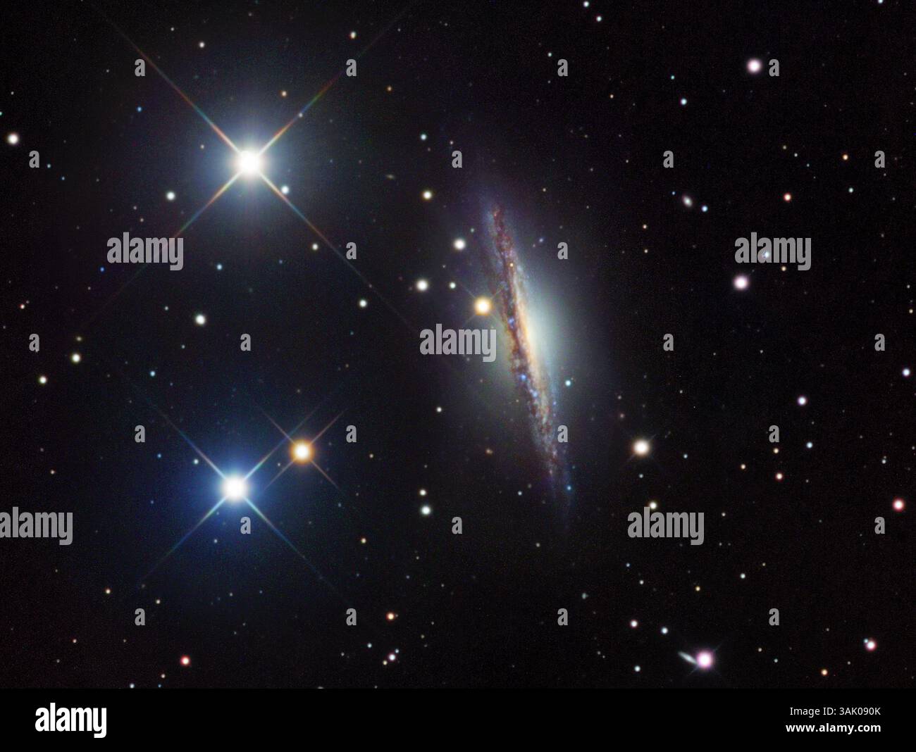 Galassia attiva NGC 1055, immagine ottica. La galassia è vista al centro. Il disco di NGC 1055 è visto come una fascia scura di polvere che attraversa il rigonfiamento centrale più luminoso. NGC 1055 è una galassia attiva che emette radiazioni dal suo nucleo, che ionizza i gas in esso contenuti e rilascia la luce che la fa brillare. Questa galassia si trova a circa 50 milioni di anni luce dalla Terra, nella costellazione Cetus. Foto Stock