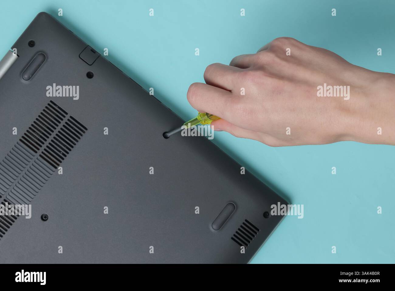 Centro di assistenza. Riparazione di notebook. Il cacciavite a mano femmina svita i bulloni del computer portatile su sfondo blu Foto Stock