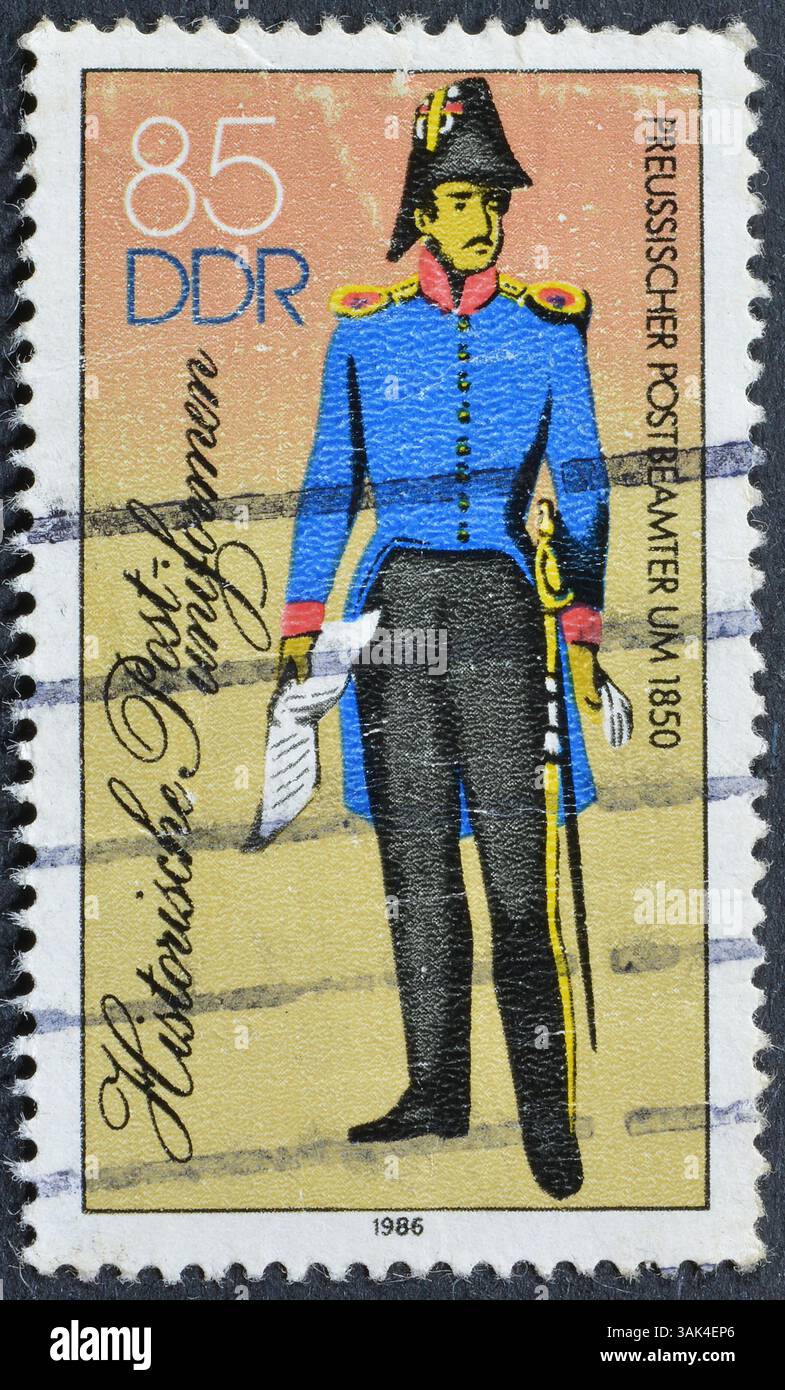Francobollo cancellato stampato dalla Germania Est, che mostra le storiche uniformi postali, intorno al 1986. Foto Stock