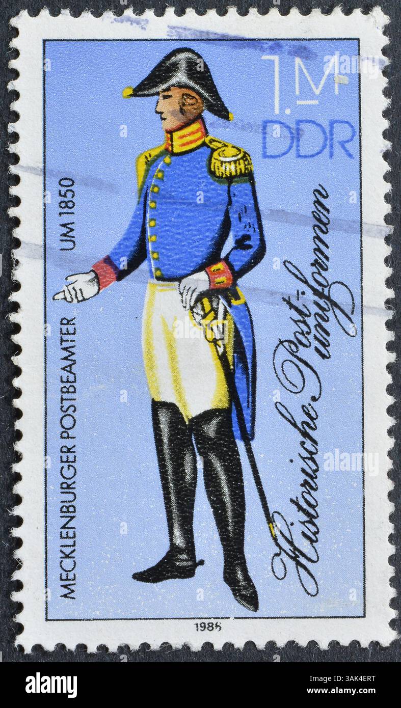 Francobollo cancellato stampato dalla Germania Est, che mostra le storiche uniformi postali, intorno al 1986. Foto Stock