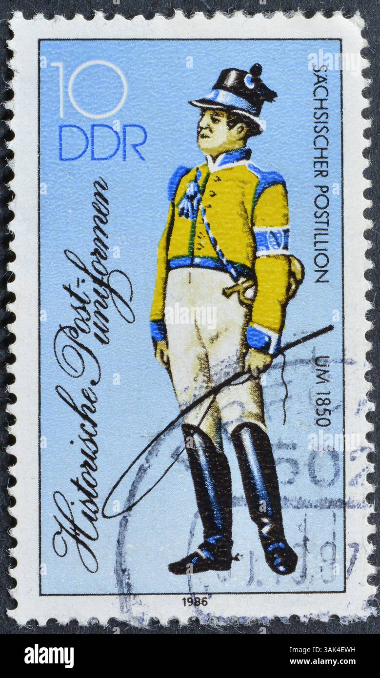 Francobollo cancellato stampato dalla Germania Est, che mostra le storiche uniformi postali, intorno al 1986. Foto Stock