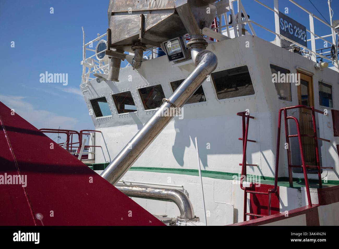 Una grande barca con uno scafo rosso e bianco e un tubo d'argento che esce dal lato. Il tubo è fissato a un grande contenitore Foto Stock