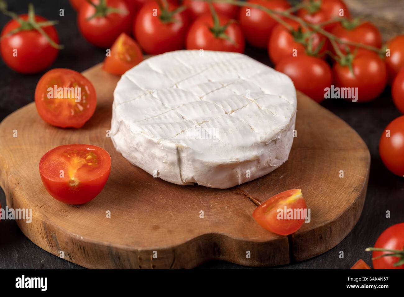 formaggio morbido con muffa e pomodori rossi maturi, un pezzo di formaggio morbido maturo e alcuni piccoli pomodori rossi rotondi sul tavolo, primo piano, vista laterale Foto Stock
