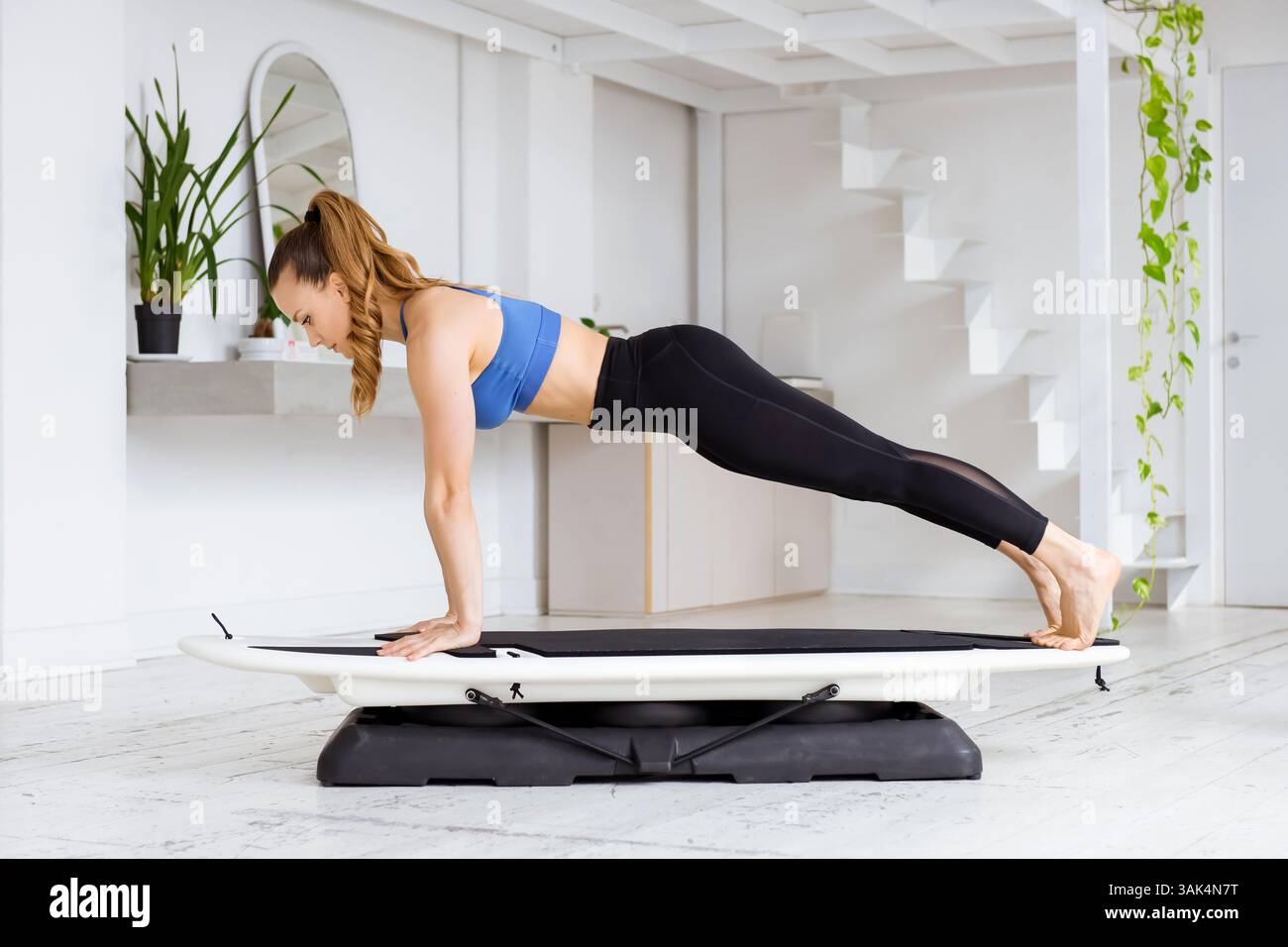 Giovane donna che esegue esercizi di rafforzamento del nucleo su Balance board in appartamento moderno, promuovendo fitness e stile di vita sano Foto Stock
