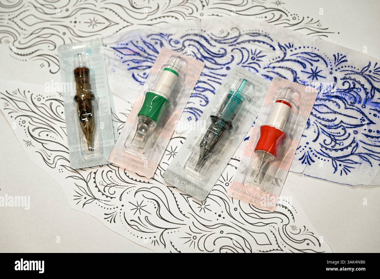 Cartucce per tatuaggi e stencil adagiati su una superficie bianca, pronti per un tatuatore a creare body art Foto Stock