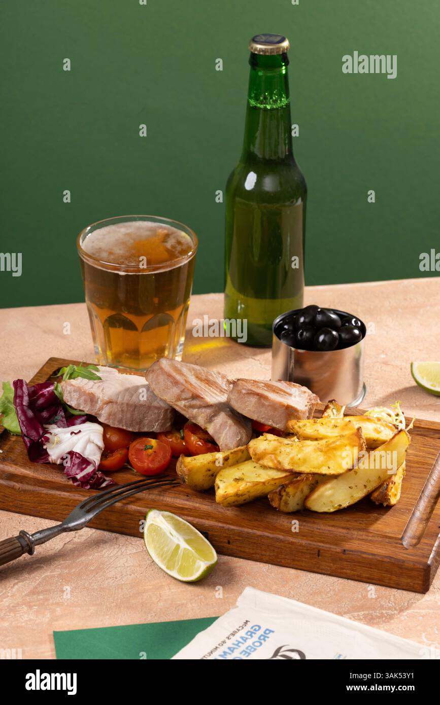 Tonno fritto su tavola di legno con altri spuntini, birra e salse in un ambiente moderno, arte culinaria. Foto di alta qualità Foto Stock