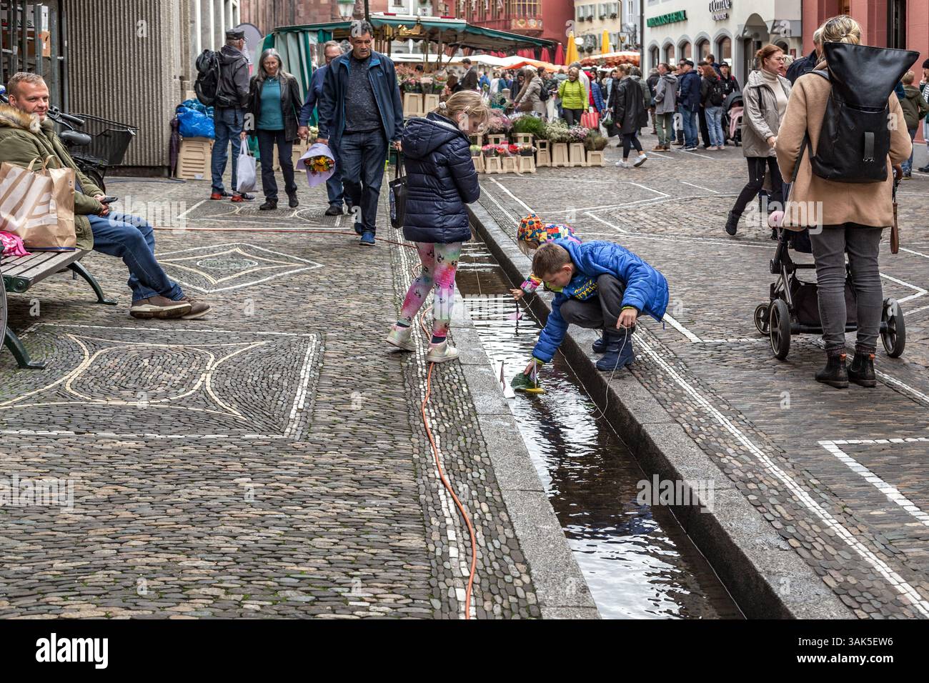 FRIBURGO Im BREISGAU, GERMANIA - 28 OTTOBRE 2023: Bambini non identificati giocano con le barche sul canale di drenaggio in Piazza della Cattedrale in un giorno di mercato. Foto Stock