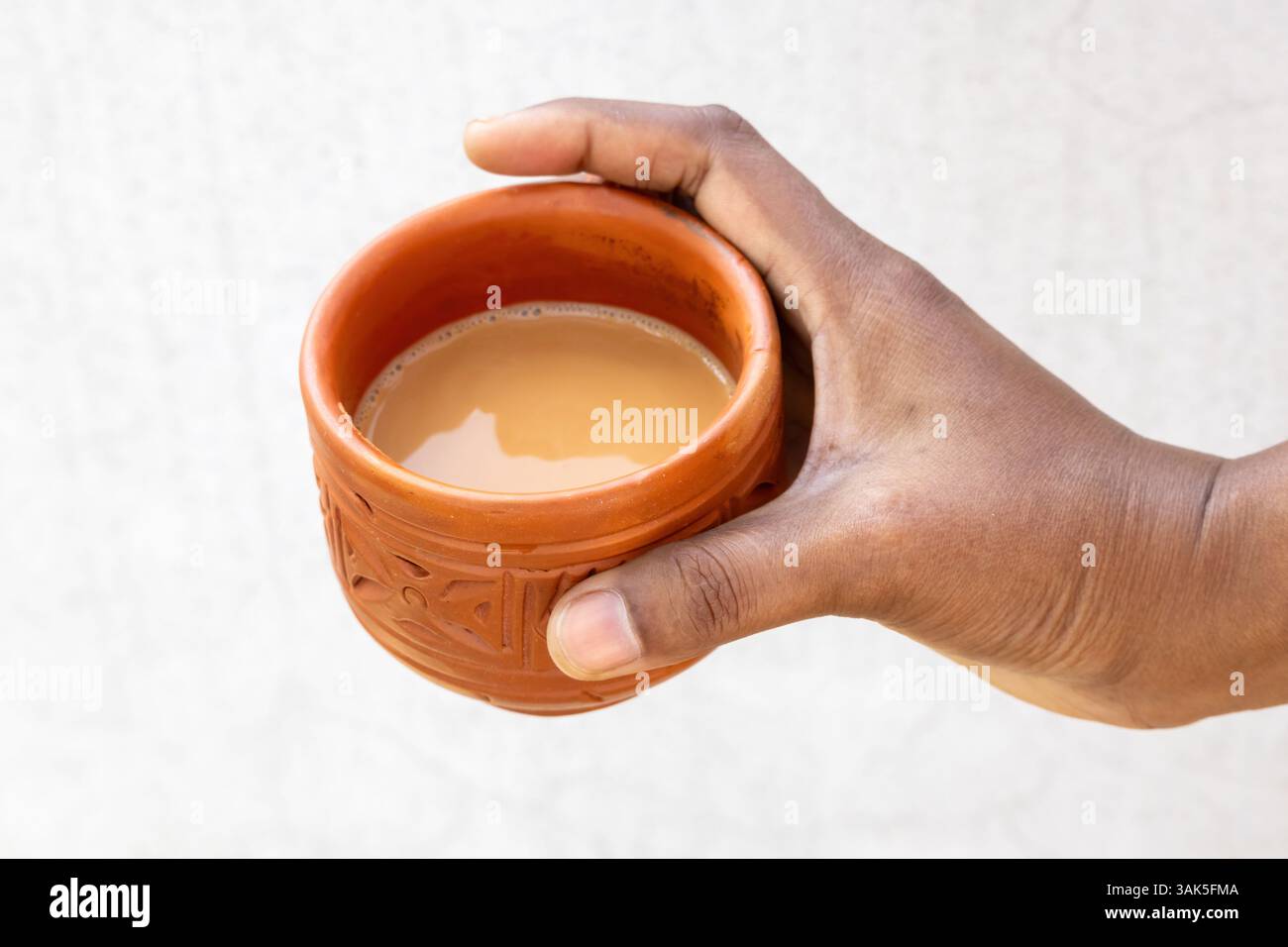 Una mano femminile tiene il tè caldo al latte, o dudh cha, in una tradizionale tazza di argilla. Foto Stock