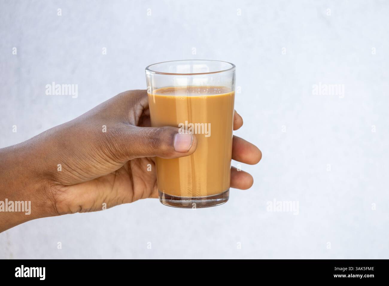 Una mano femminile regge una tazza di tè al latte caldo, o dudh cha, su uno sfondo bianco sfocato. Foto Stock