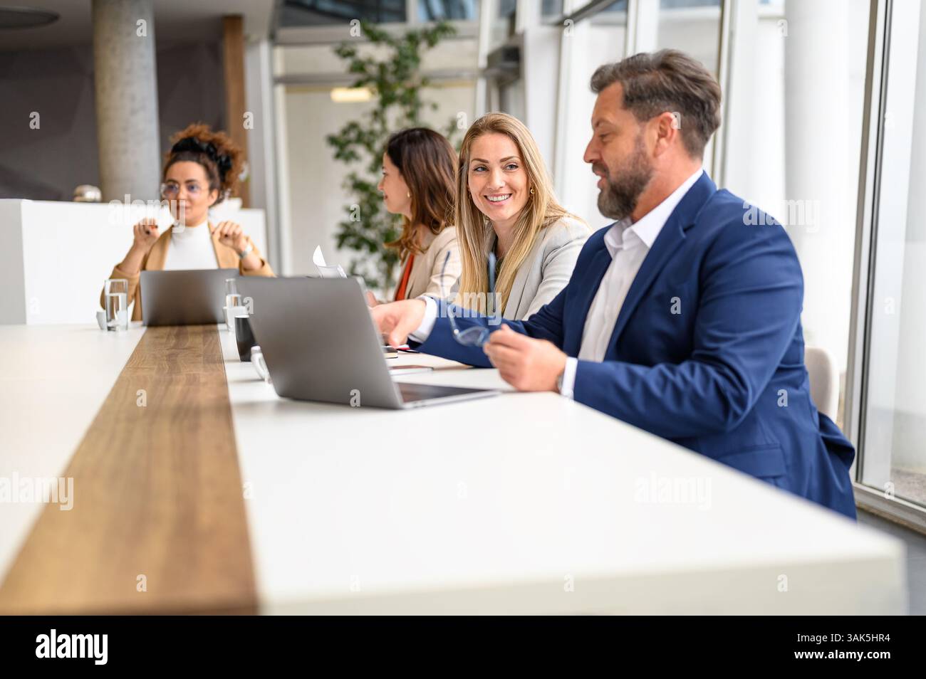 Uomo d'affari che lavora su un laptop e che discute idee con una collega durante una riunione in ufficio Foto Stock
