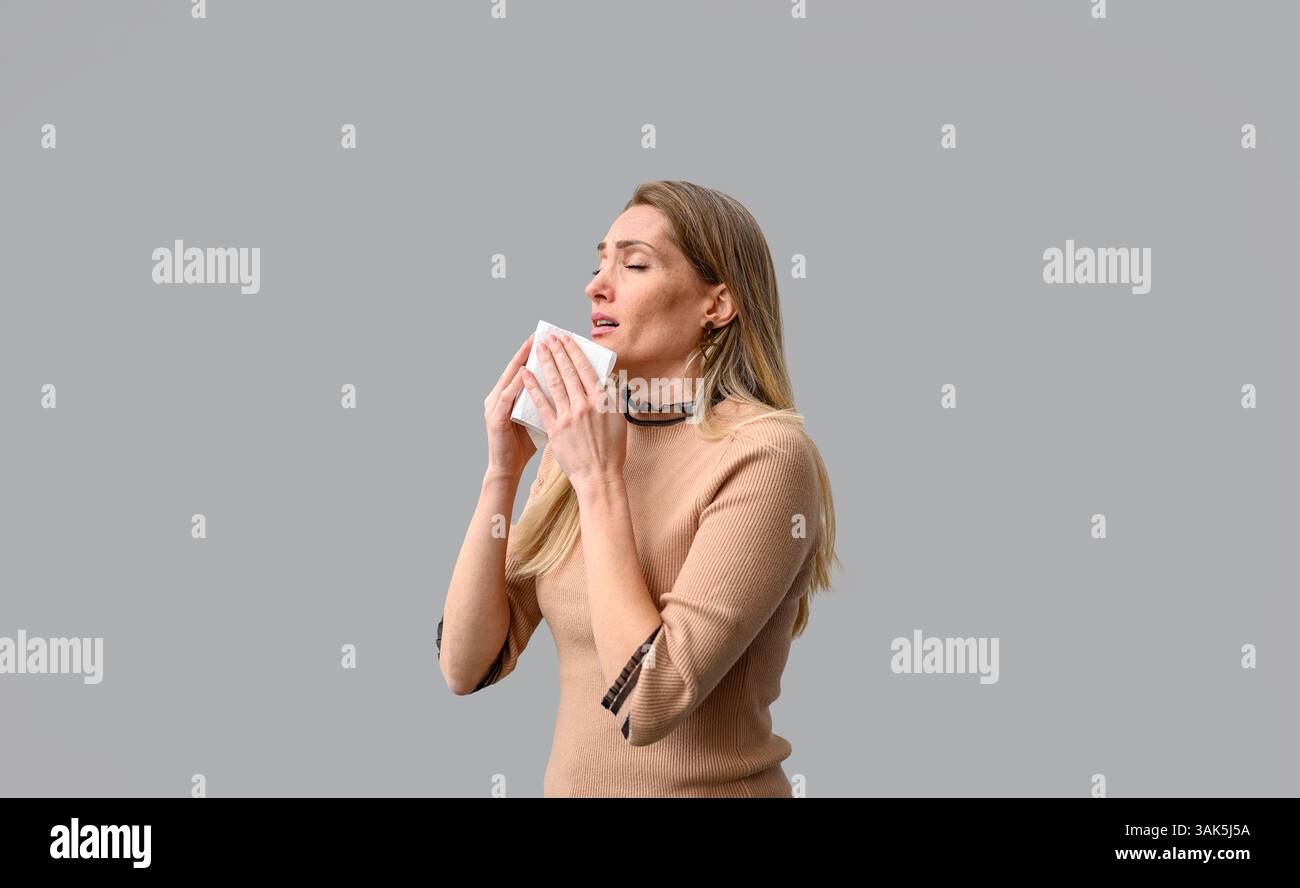 Ritratto di una giovane donna che tiene il fazzoletto con gli occhi chiusi e si prepara a starnutire a causa del freddo su sfondo bianco Foto Stock