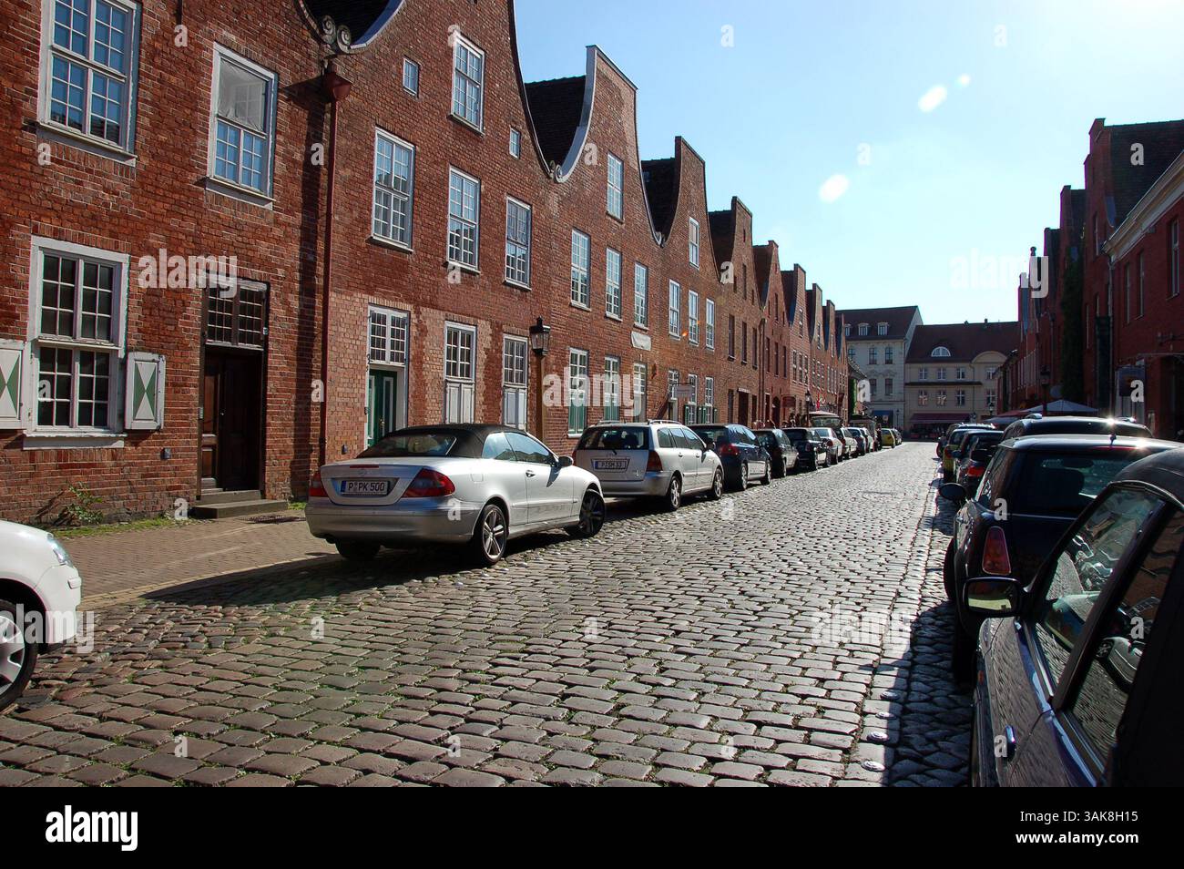 Tradizionali case in mattoni rossi nel quartiere olandese (Holländisches Viertel) di Potsdam, Germania, che costeggiano una strada acciottolata con auto parcheggiate in una giornata di sole Foto Stock