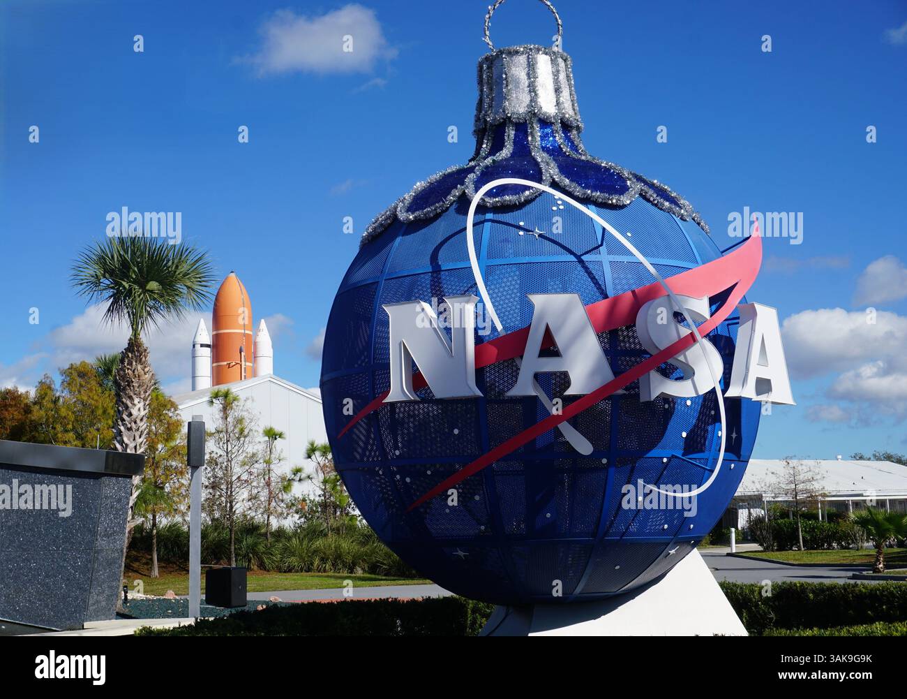 Un globo metallico blu con il logo della NASA si trova all'ingresso del Kennedy Space Center, Cape Canaveral, Florida, con lo Space Shuttle sullo sfondo Foto Stock