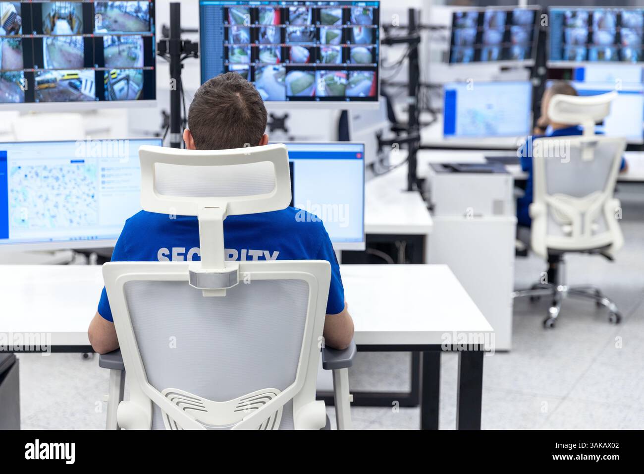 Agente di sicurezza che monitora più schermi di sorveglianza in una sala di controllo high-tech per la sicurezza e la sorveglianza Foto Stock
