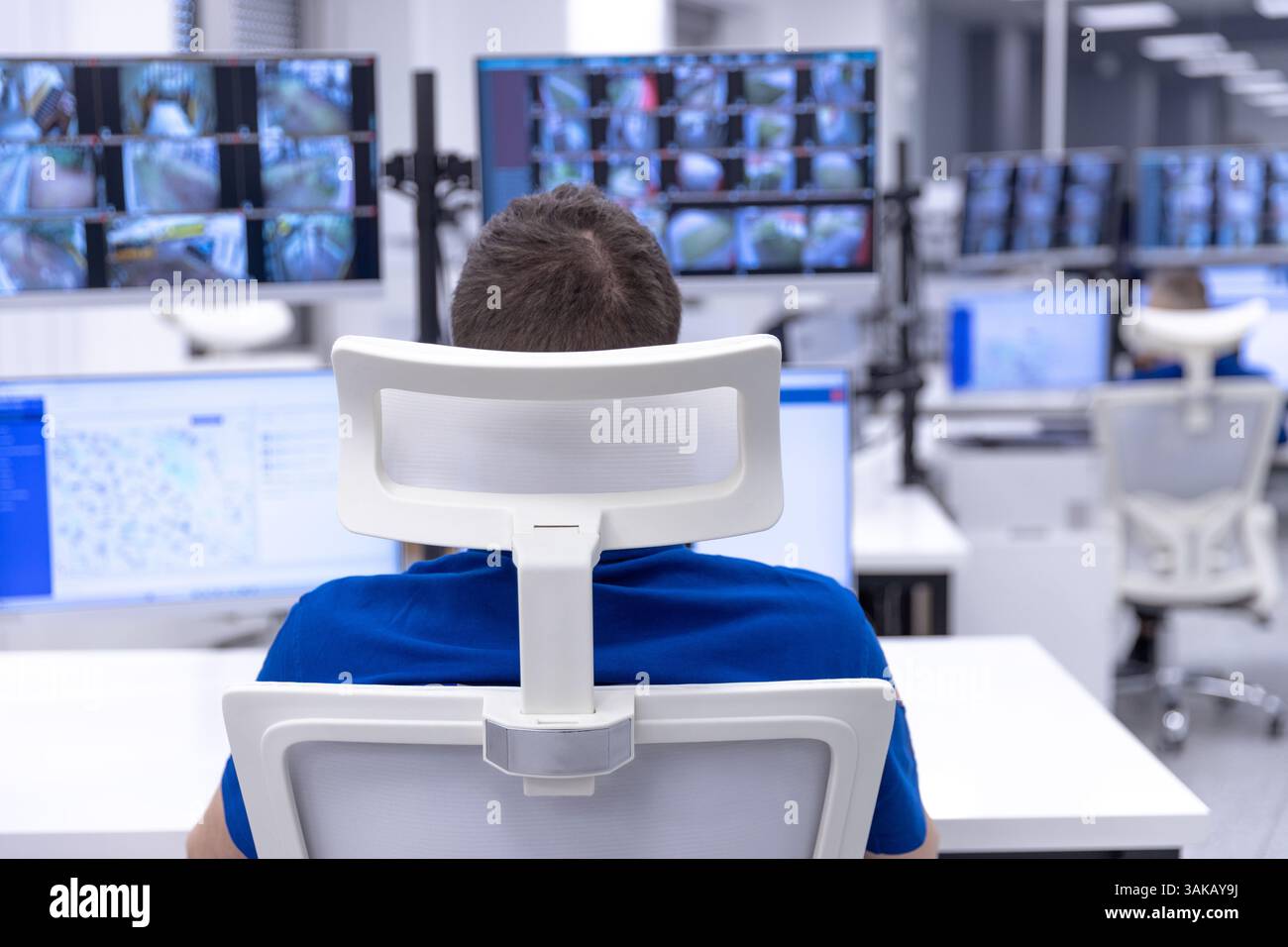 Agente di sicurezza che monitora più schermi di sorveglianza in una sala di controllo high-tech per la sicurezza e la sorveglianza Foto Stock