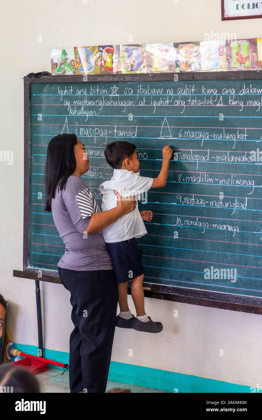 Insegnante di scuola elementare pubblica a Batangas, Filippine, insegna ai suoi studenti in una classe, sottolineando il valore dell'istruzione pubblica e della dedica Foto Stock