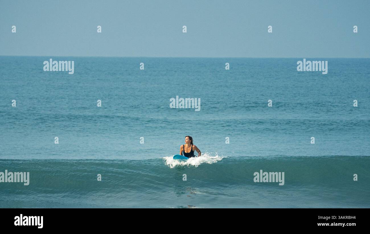 Una donna che naviga su un'onda pulita a Varkala Beach, Kerala, India. Scattata con una fotocamera mirrorless Alpha A7 III di Sony, che mette in mostra l'emozione e la bellezza di c Foto Stock