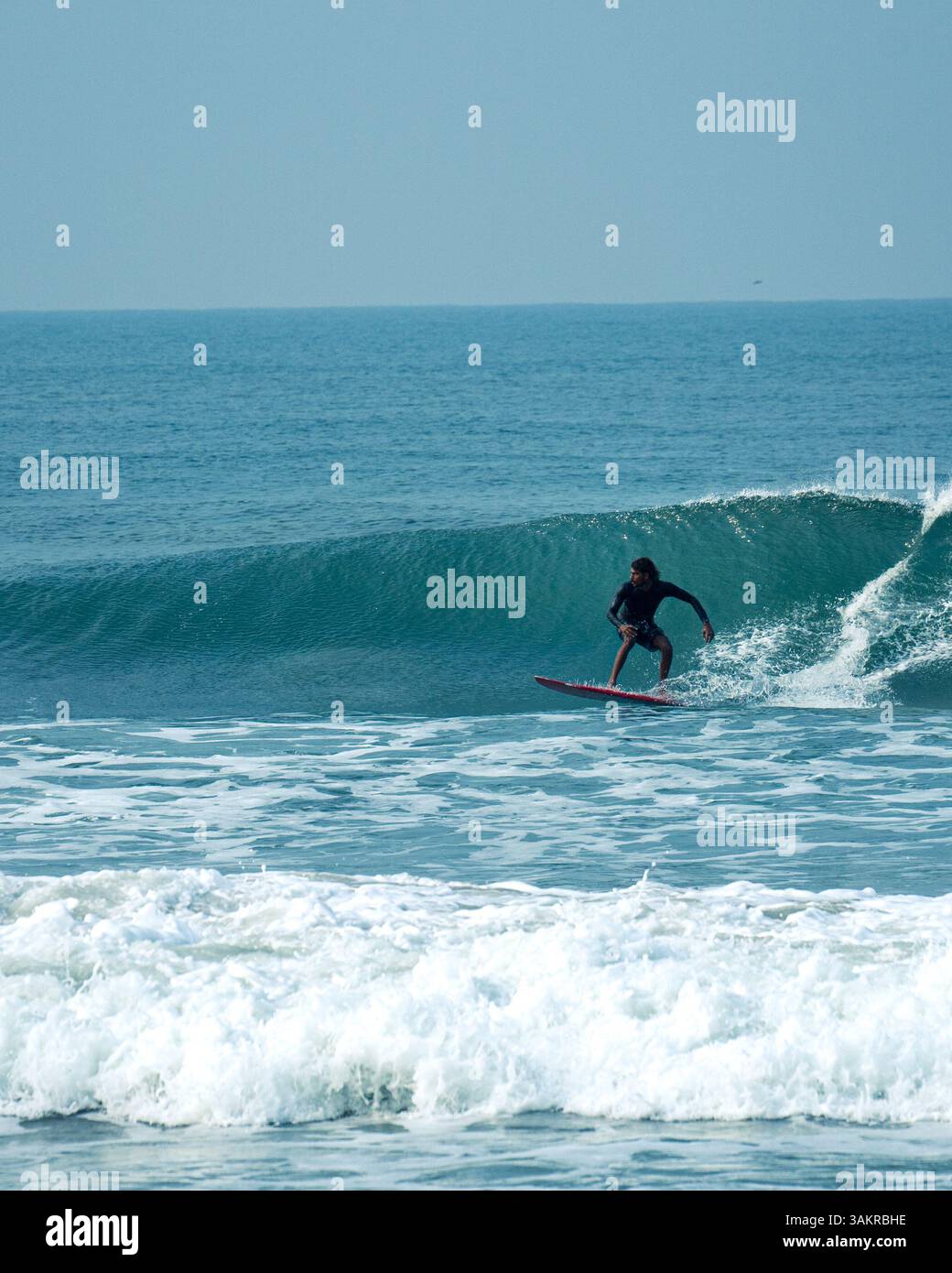 Un uomo che naviga su un'onda pulita a Varkala Beach, Kerala, India. Ripresa con una fotocamera mirrorless Alpha A7 III di Sony Foto Stock