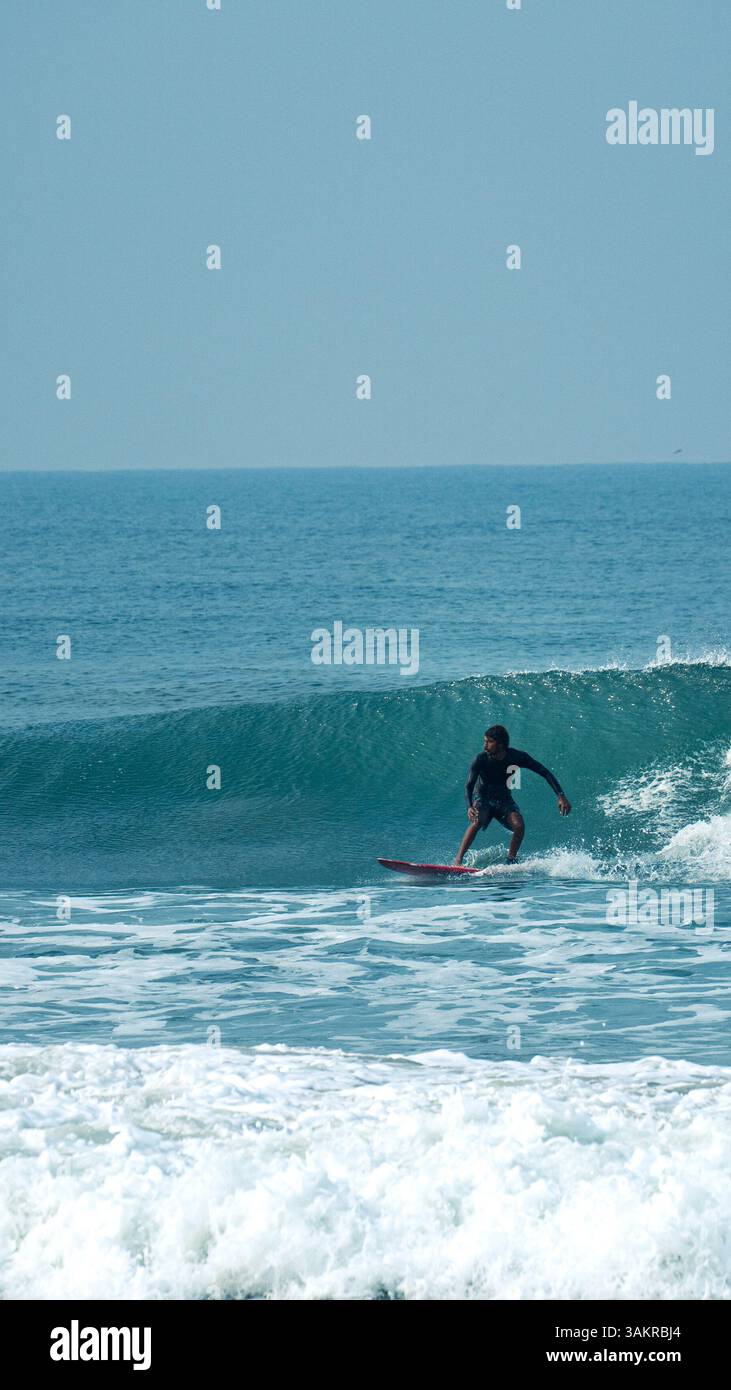 Un uomo che naviga su un'onda pulita a Varkala Beach, Kerala, India. Ripresa con una fotocamera mirrorless Alpha A7 III di Sony Foto Stock