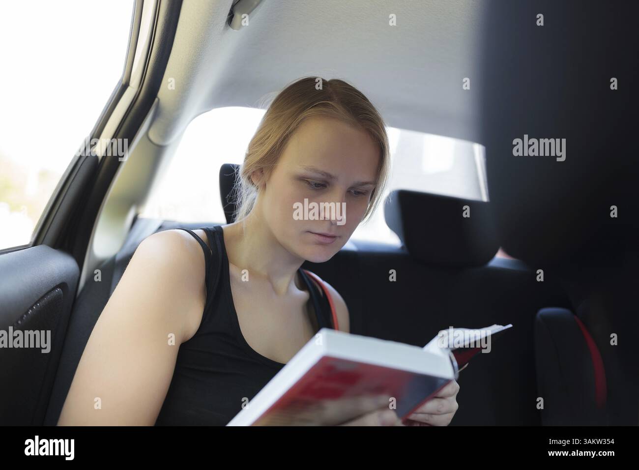 Giovane donna a leggere un libro mentre si viaggia su un sedile posteriore della vettura Foto Stock