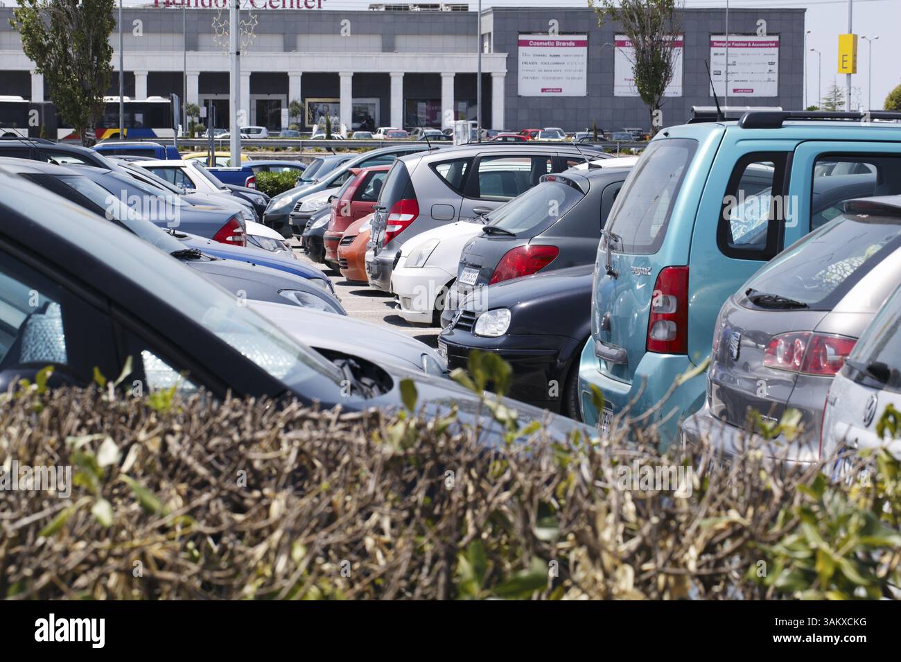 SALONICCO, GRECIA - 1° AGOSTO 2013: Vista su una siepe di auto ben affollate parcheggiate in un parcheggio all'aperto al sole di fronte a un'azienda commerciale Foto Stock