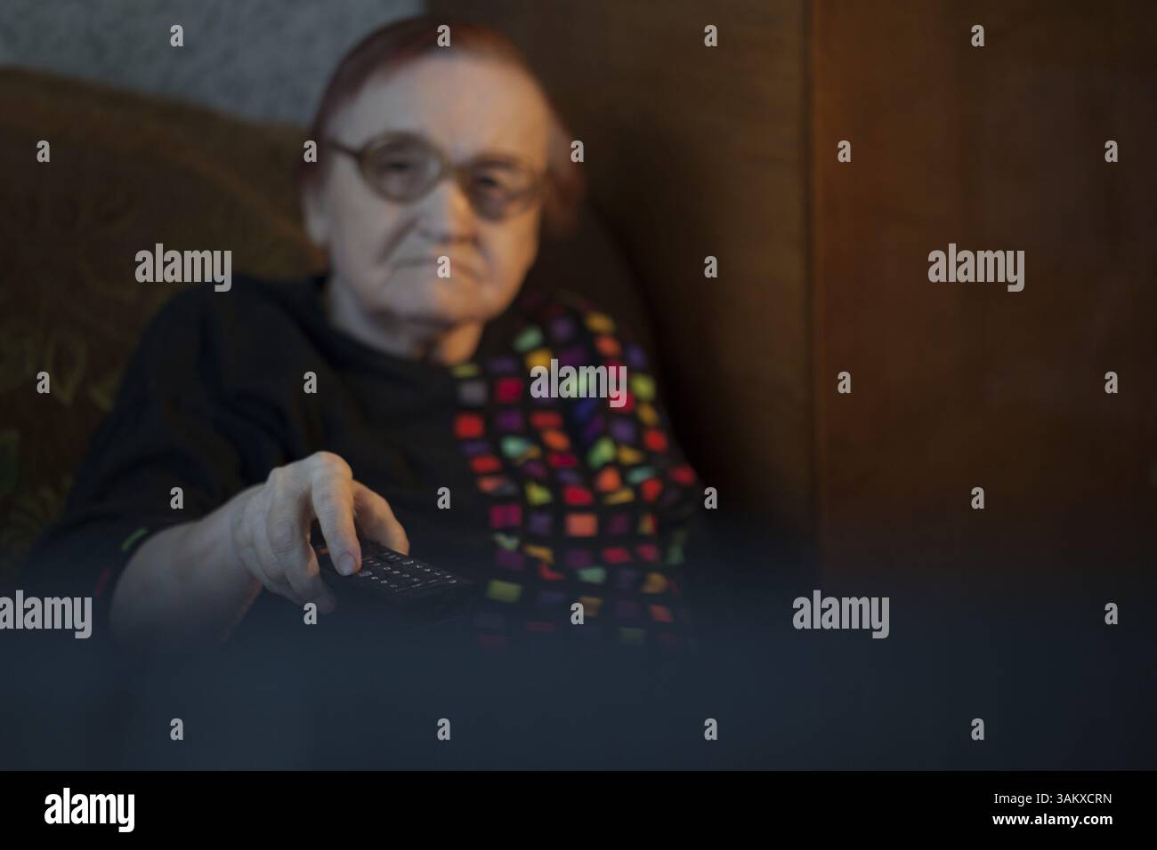 Vista da dietro il televisore di una signora anziana guardando la televisione tramite il telecomando per cambiare i canali Foto Stock