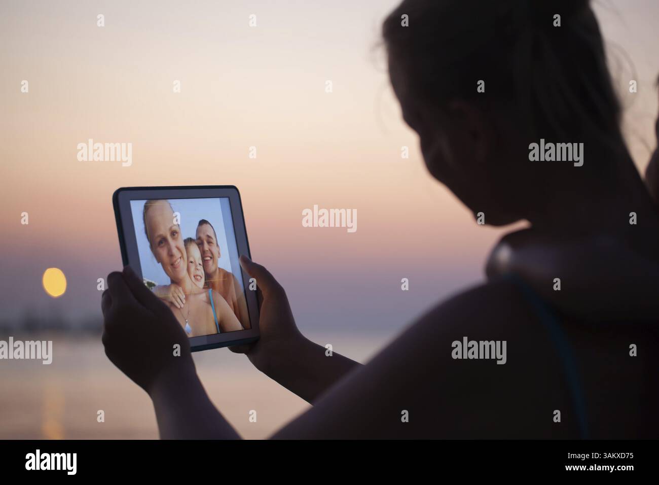 Rendendo selfie della famiglia usando il touch pad. Felice madre, padre e figlio piccolo sulla spiaggia al tramonto Foto Stock