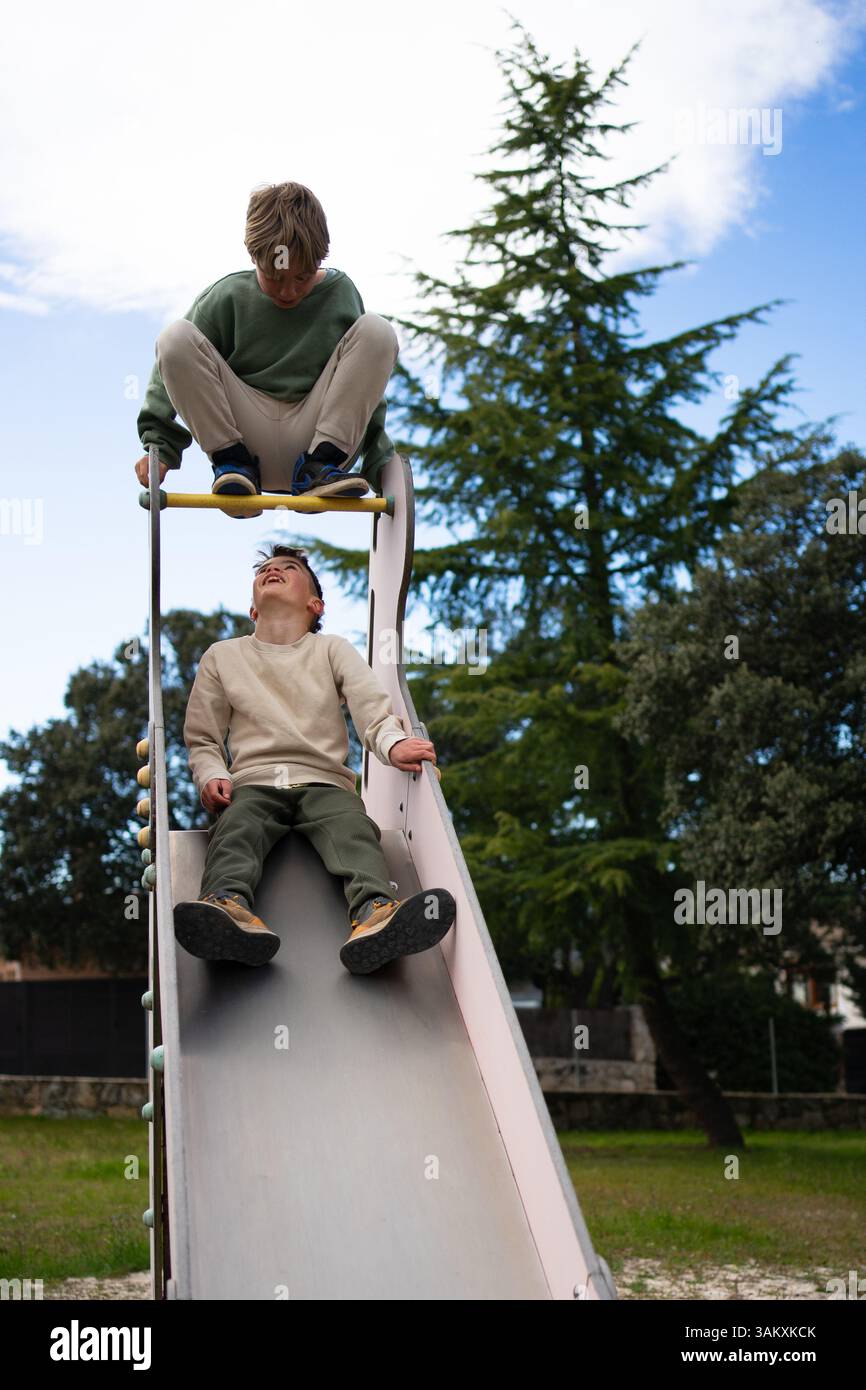 Due fratelli giocano su uno scivolo in un parco giochi durante una giornata estiva Foto Stock