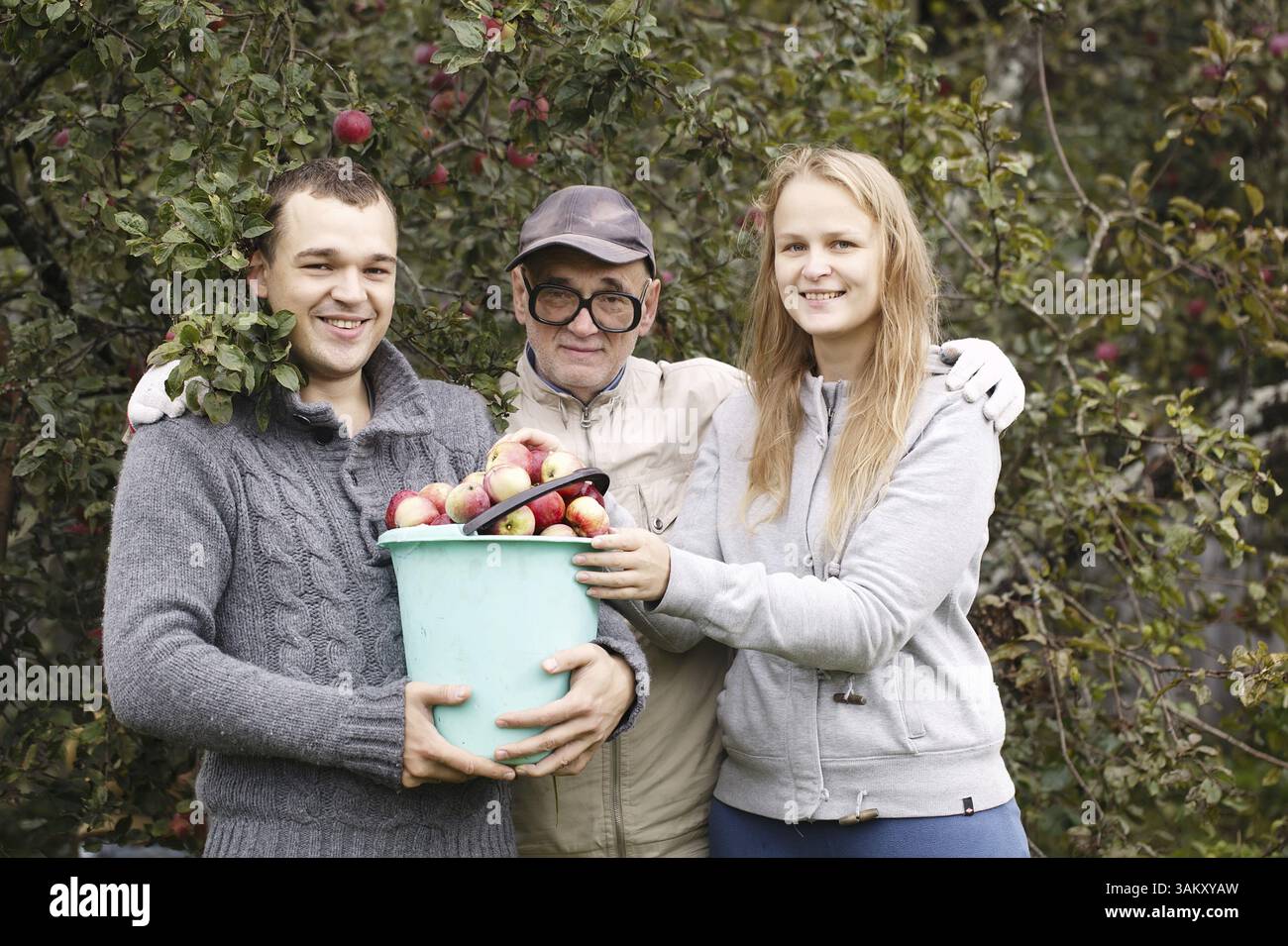 Marito, moglie e nonno con un fruttifero. Uomo che tiene un secchio pieno di mele fresche, donna che mette un po' di frutta in cima, tutto guardando al fotogra Foto Stock