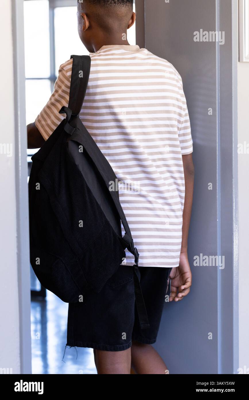 Entrando in classe, studente con zaino che indossa camicia a righe e pantaloncini corti Foto Stock