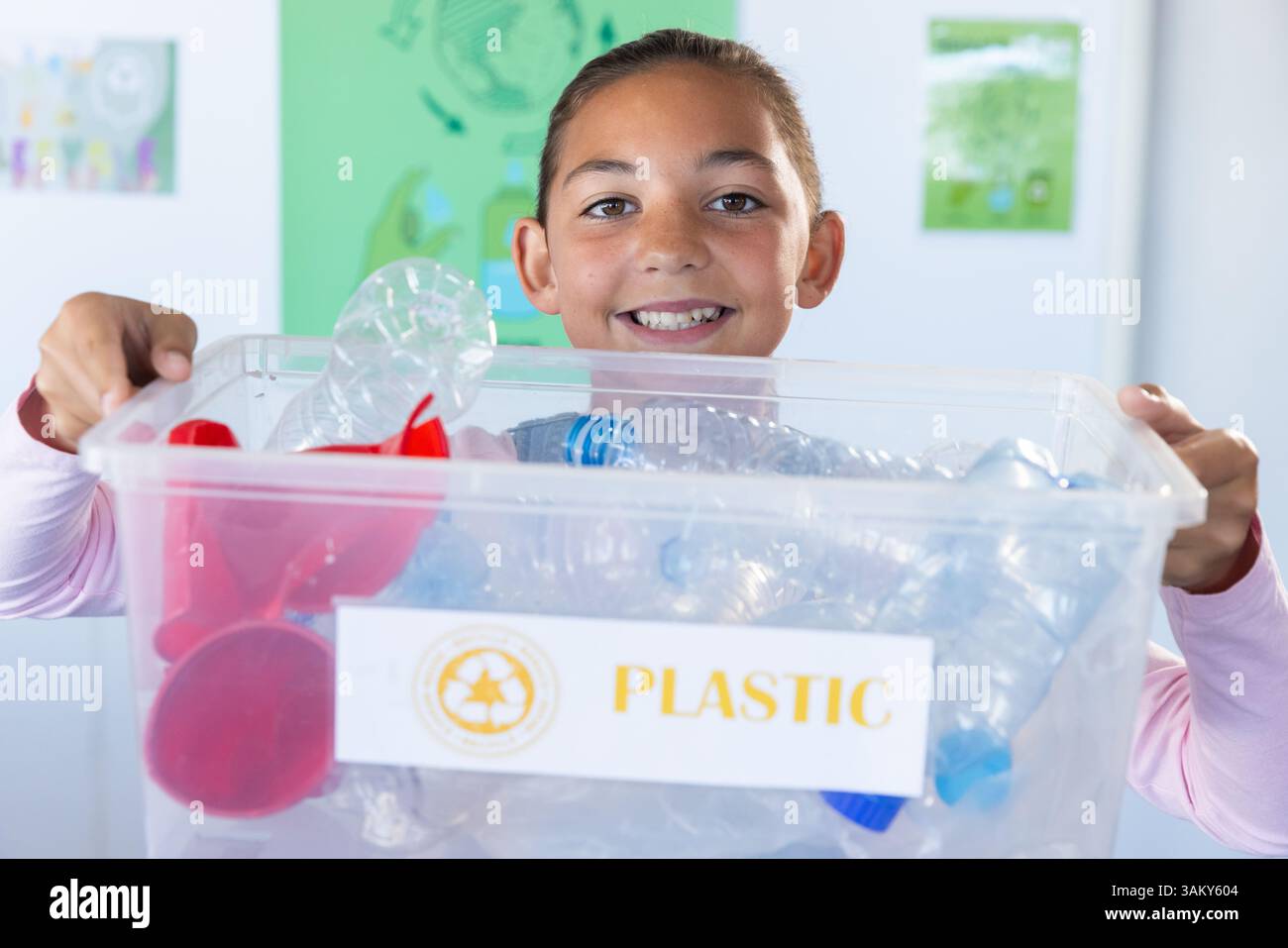 Tenendo in mano il cestino di riciclaggio, sorridente ragazza che partecipa al programma di riciclaggio scolastico Foto Stock