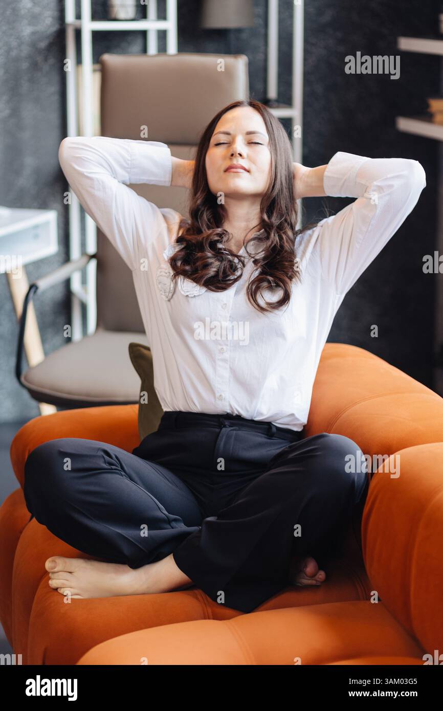 Una donna su una sedia da ufficio si appoggia alla schiena a occhi chiusi, prendendosi una pausa per rilassarsi e ridurre lo stress sul posto di lavoro. Foto Stock