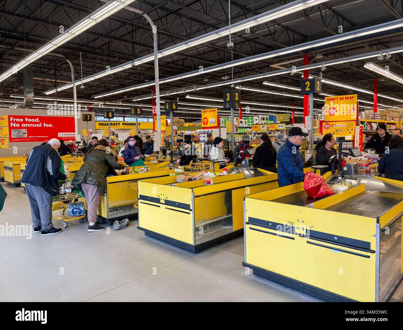 Una scena movimentata all'interno di un supermercato No Frills in Canada, che mostra gli acquirenti in fila ai banchi di cassa gialli con la spesa. Foto Stock