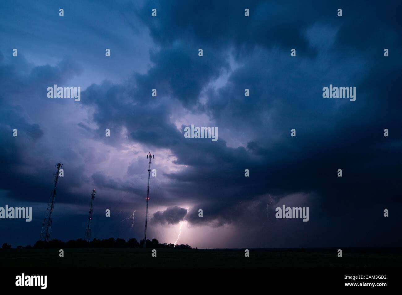 Un fulmine spettacolare durante un temporale notturno illumina le nuvole scure sopra le torri cellulari in un paesaggio rurale. Il cielo intenso e il fulmine Foto Stock
