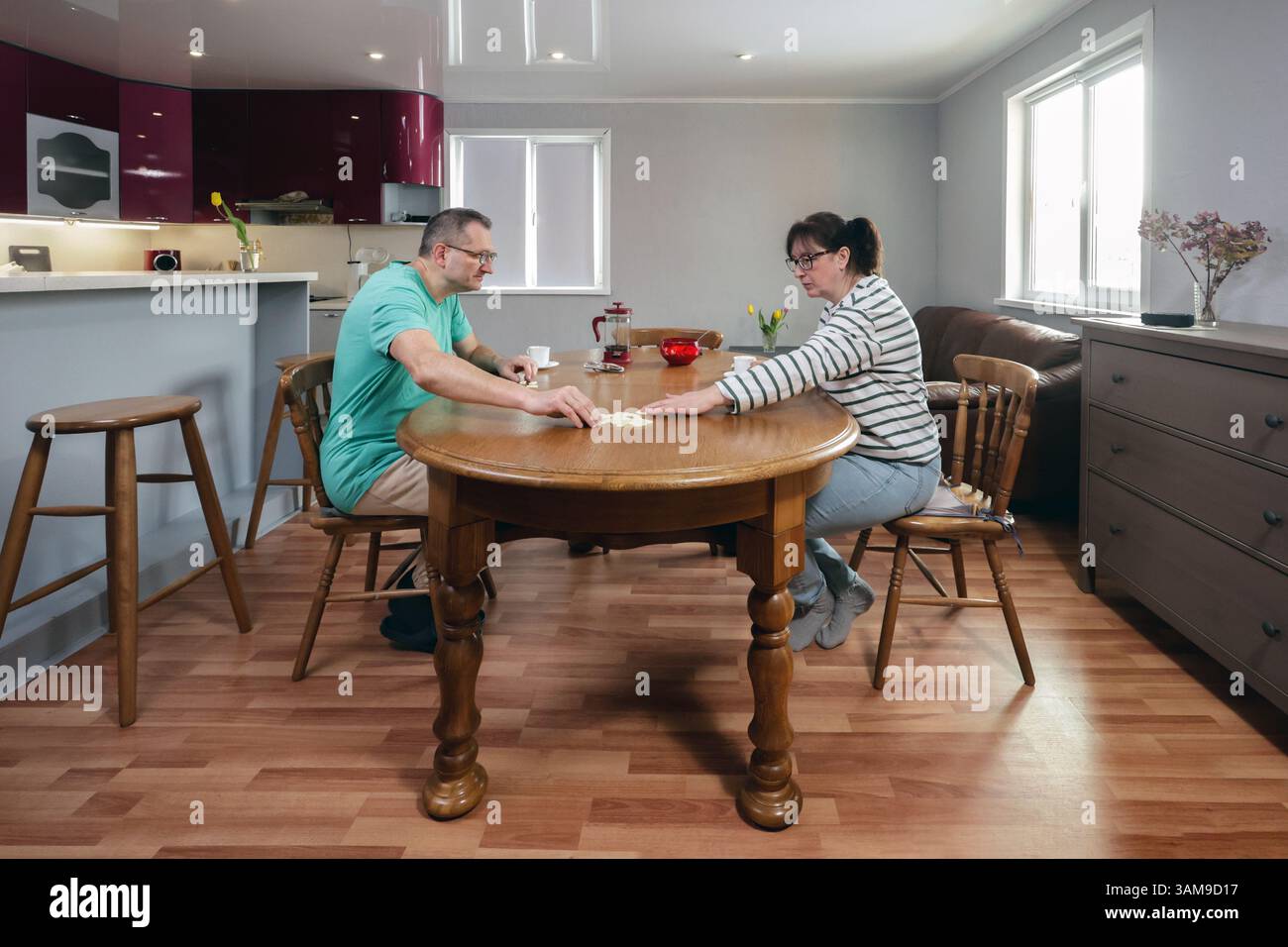 La coppia si concentra sul gioco del domino, seduto l'uno dall'altro a tavola in casa, concentrandosi sulla strategia per la prossima mossa, bevendo un caffè nelle vicinanze. Foto Stock