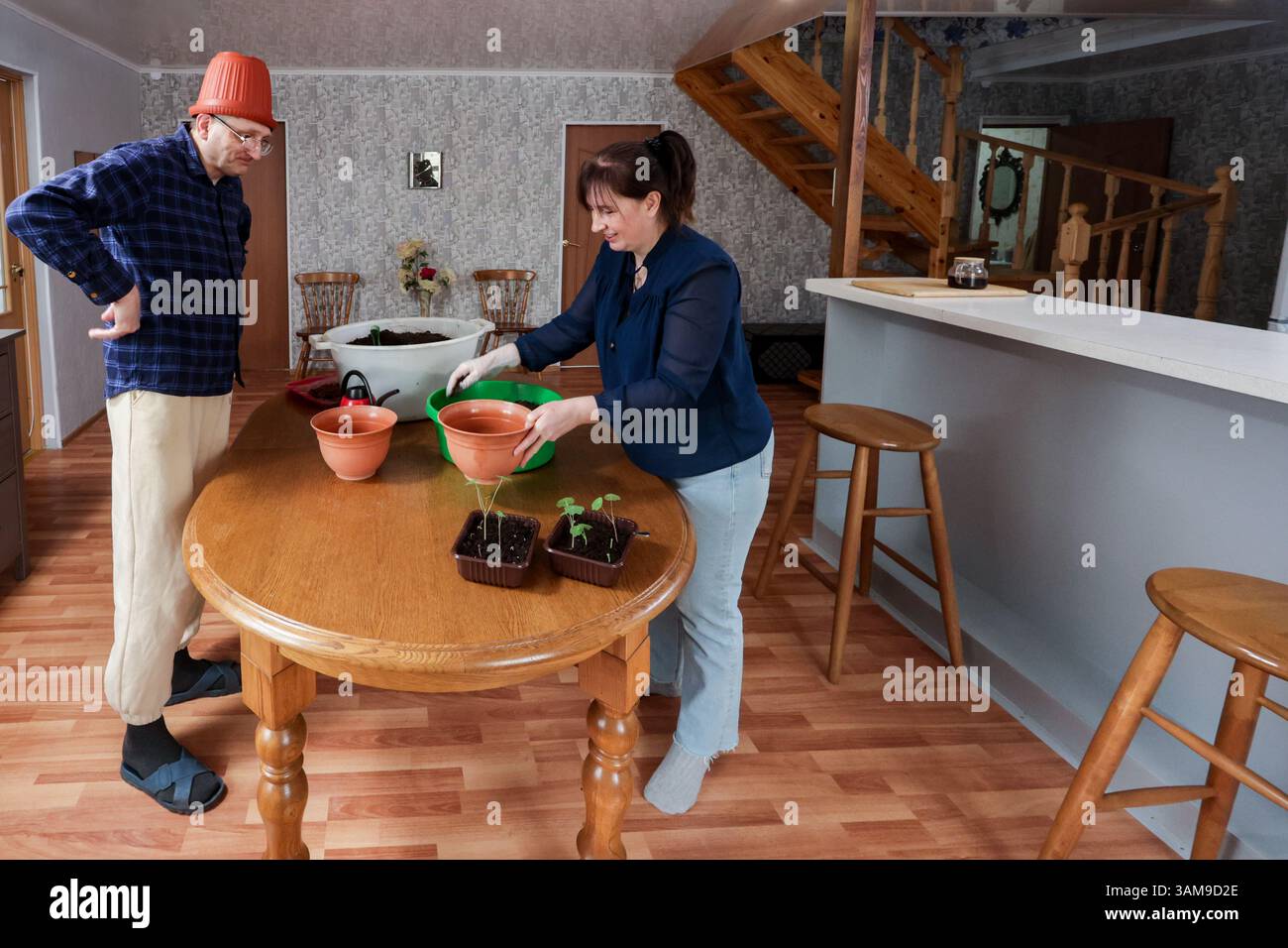 Mentre trapiantando con cura le piantine in vasi a casa, la coppia matura negli anni '50 condivide un momento di calma, l'uomo indossa un vaso di fiori sulla testa probabilmente per divertimento. Foto Stock