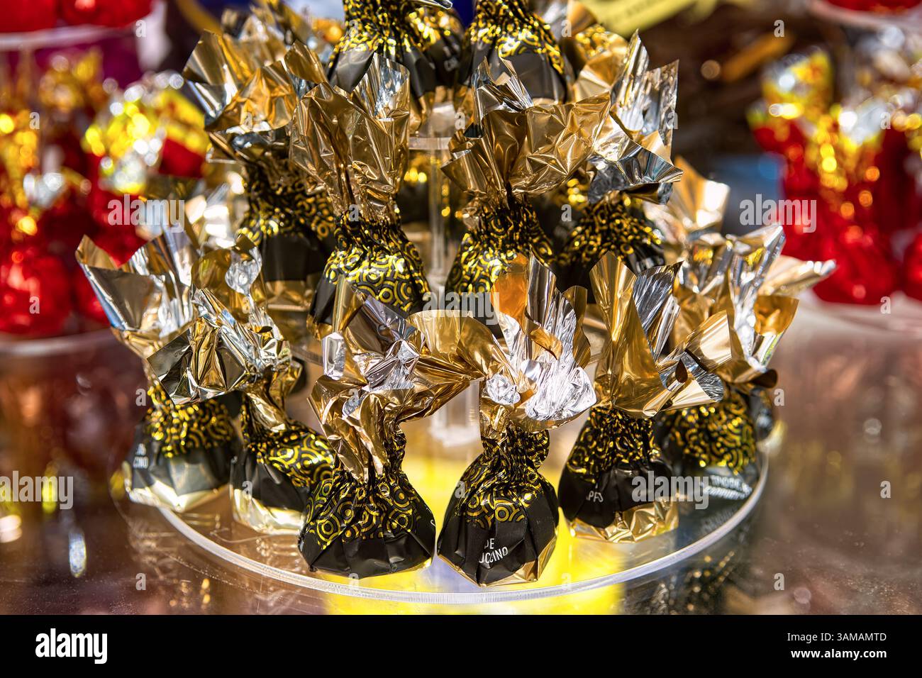 Caramelle al tartufo di cioccolato in lucidi involucri su banco di vetro nella vetrina della pasticceria. Foto Stock
