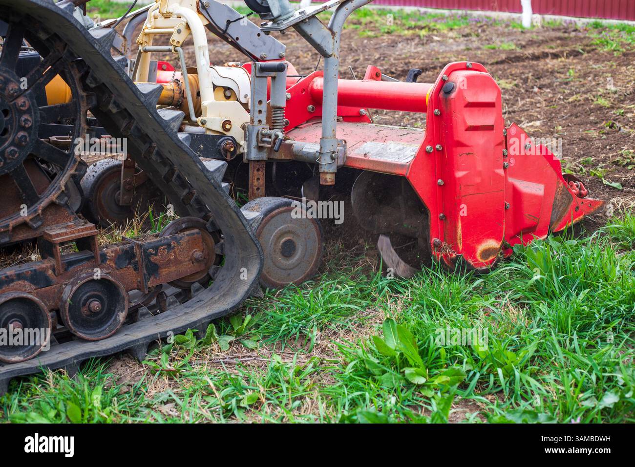 Primo piano di un trattore cingolato con un coltivatore montato che lavora su terreni agricoli. Coltivazione del suolo, tecnologia agricola. Foto Stock