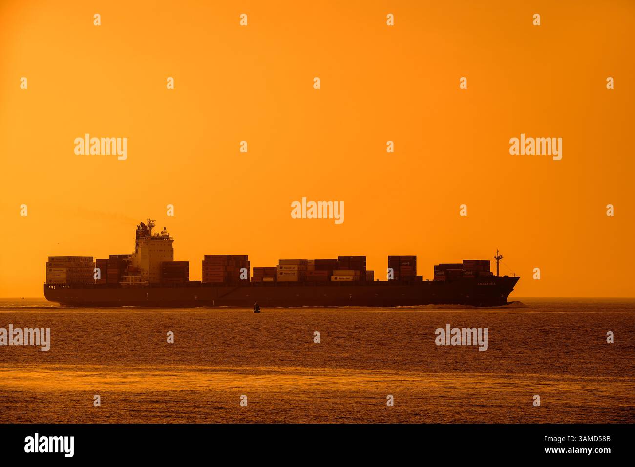 Nave portacontainer/container Amalthea, caricata con contenitori sagomati contro il cielo arancione del tramonto Foto Stock