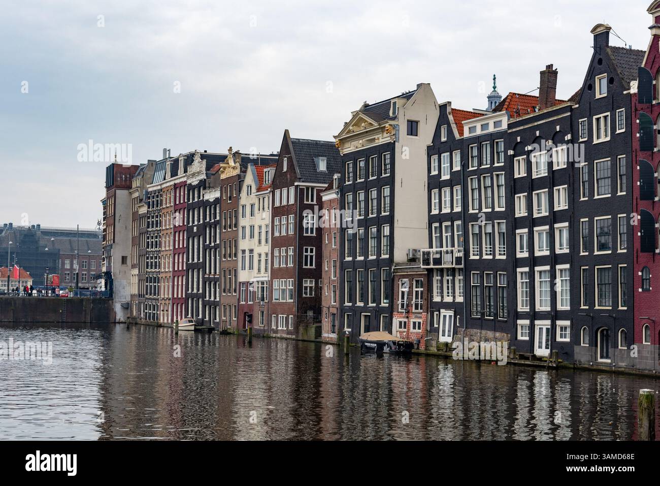 Fila di case tradizionali olandesi colorate e strette che si riflettono su un canale di amsterdam, nei paesi bassi, sotto un cielo nuvoloso Foto Stock