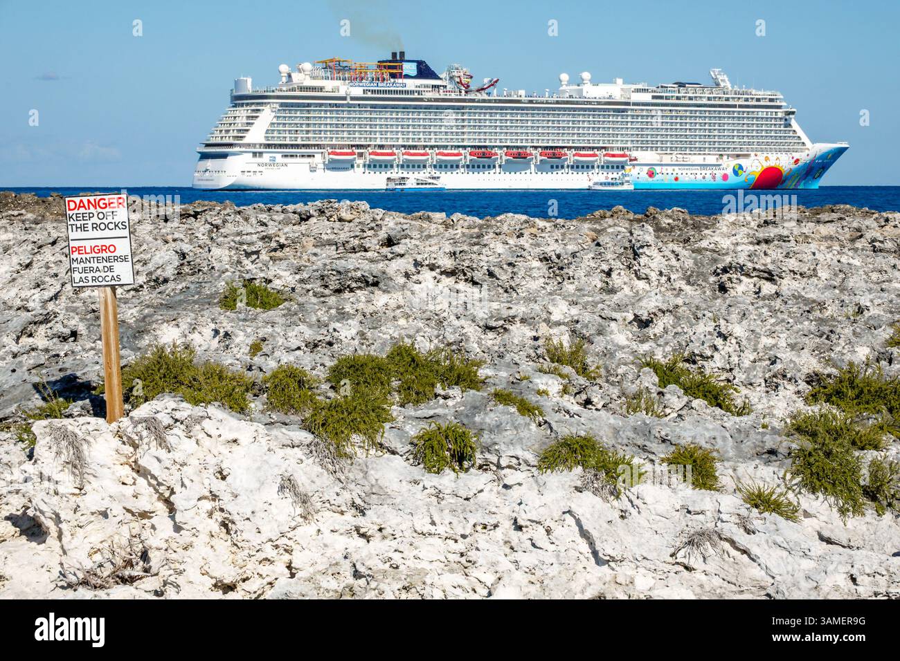 Great Stirrup Cay The Bahamas, costa rocciosa dell'oceano, cartello DI PERICOLO "TENERE lontano DALLE ROCCE", cartello di avvertimento inglese spagnolo, terreno roccioso vulcanico, sicurezza costiera Foto Stock