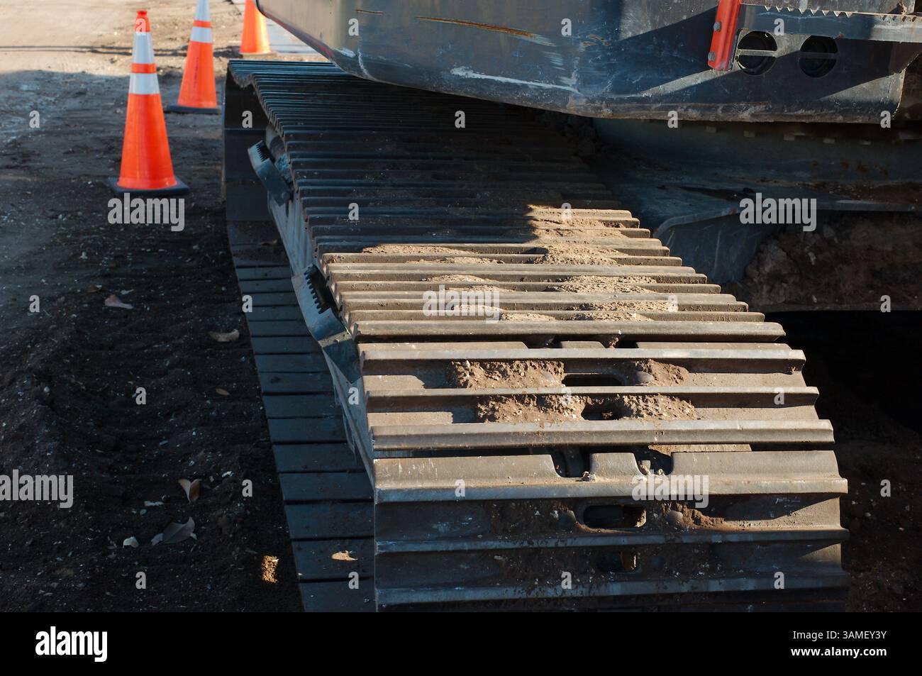 Attrezzature per l'edilizia pesante in un cantiere con coni per il traffico. Primo piano di macchinari cingolati per impieghi gravosi in un cantiere, con coni stradali inseriti Foto Stock