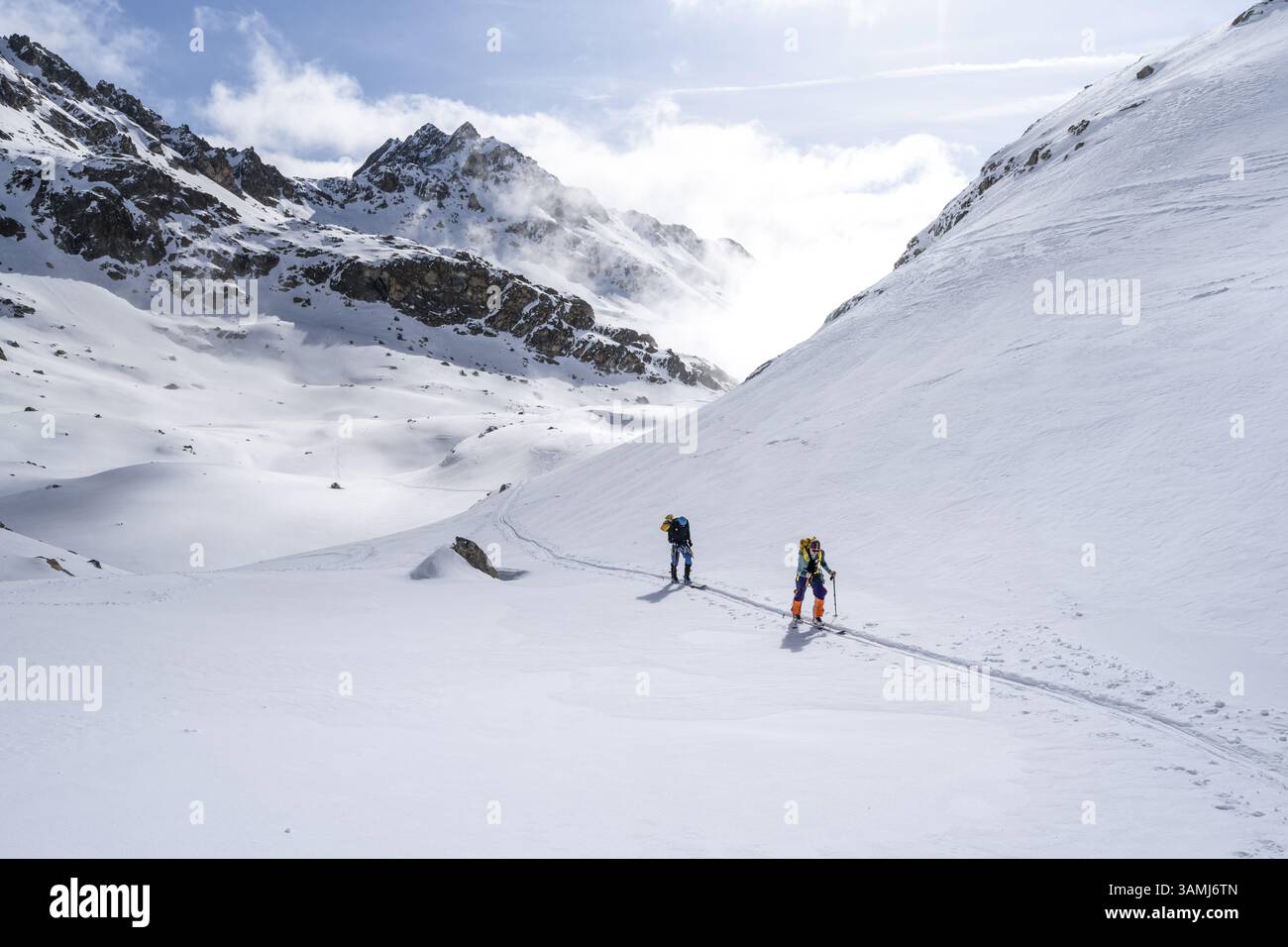Nuvole d'atmosfera in un paesaggio montano ventoso, sciatori sulla salita a porta d'es-cha, tour sciistico del Grigioni Haute Route, Alpi Albula, Retico al Foto Stock